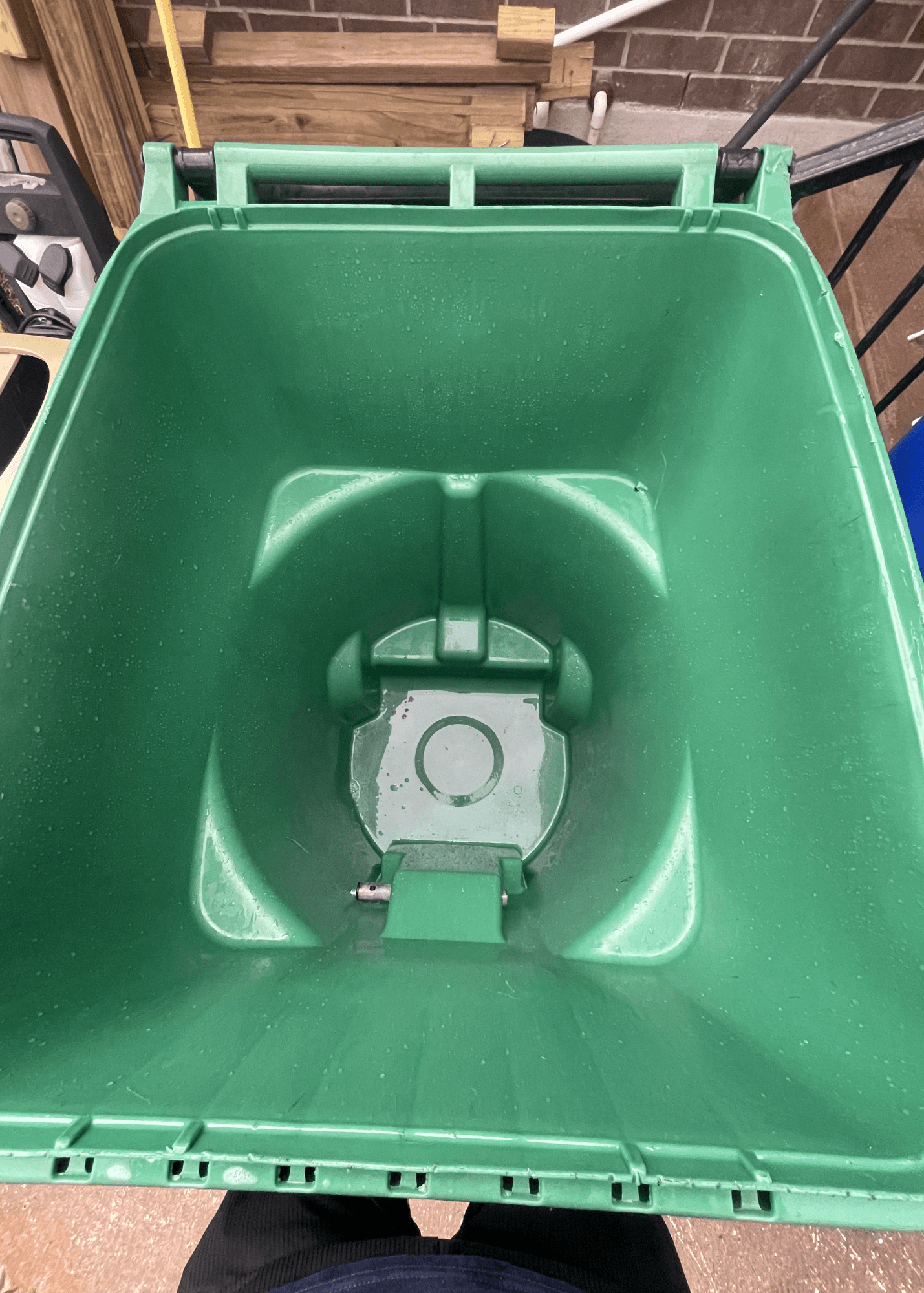 Empty green plastic waste bin interior with water droplets and a molded base design.