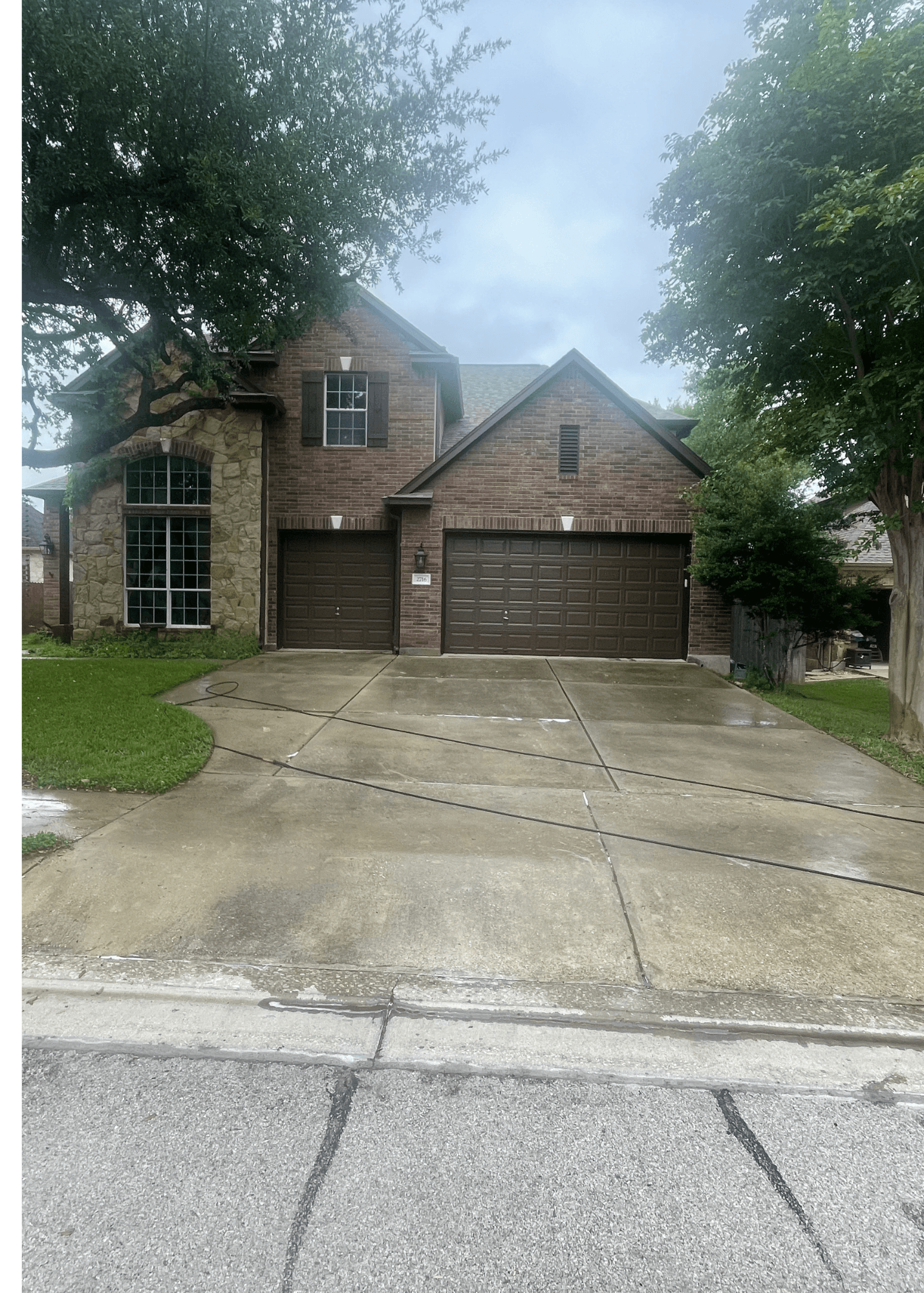 Suburban brick home with stone accents, brown garage doors, and a wet concrete driveway.