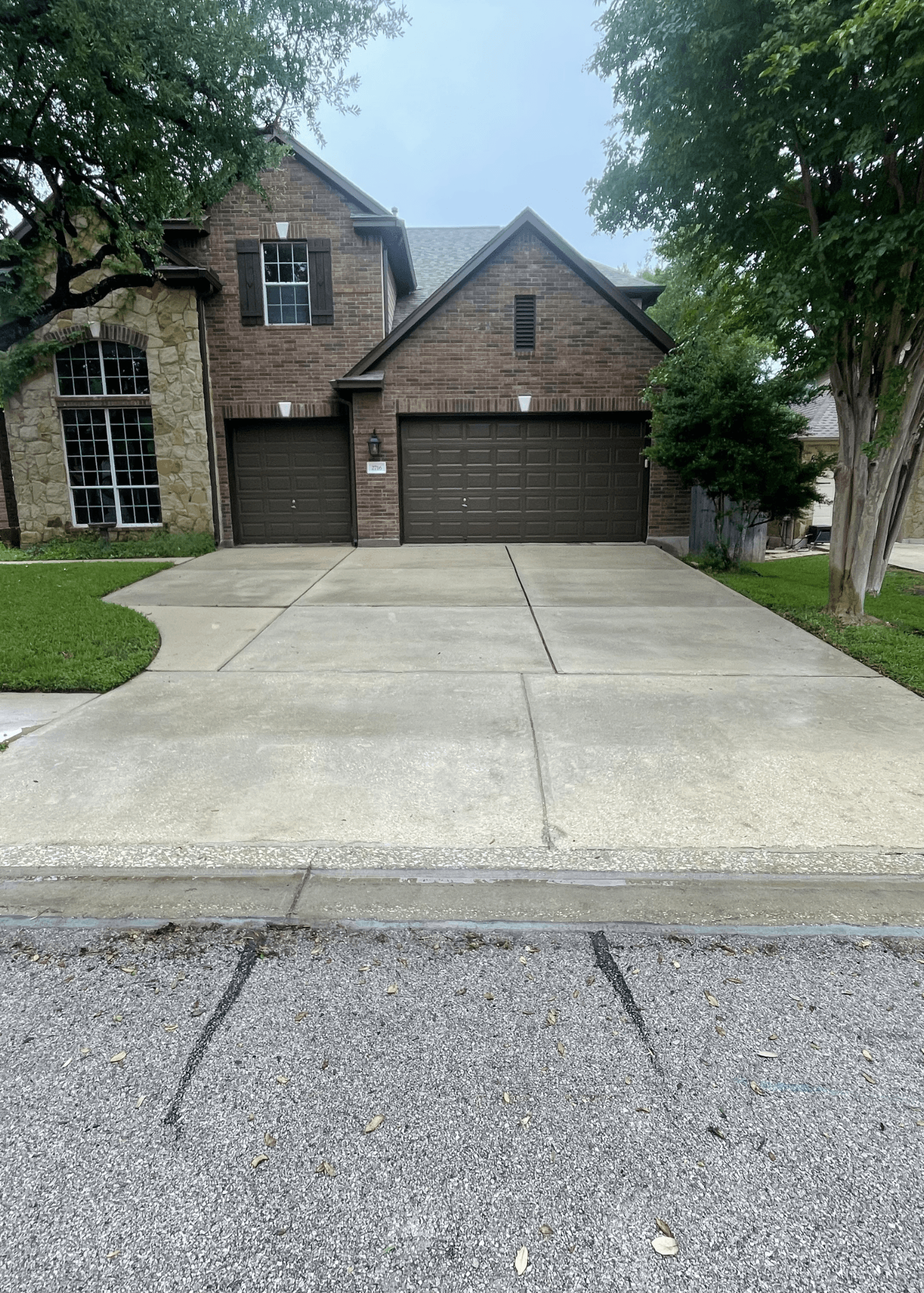Brick and stone house with a large concrete driveway and two dark brown garage doors.