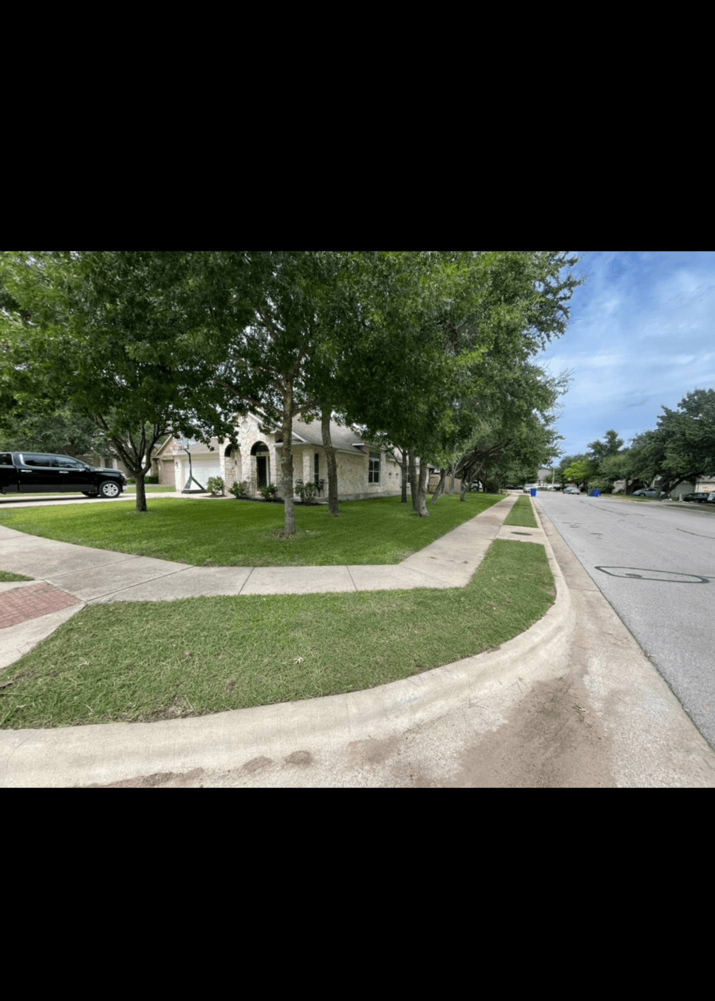 White stone house with a green lawn and large trees on a suburban street corner.